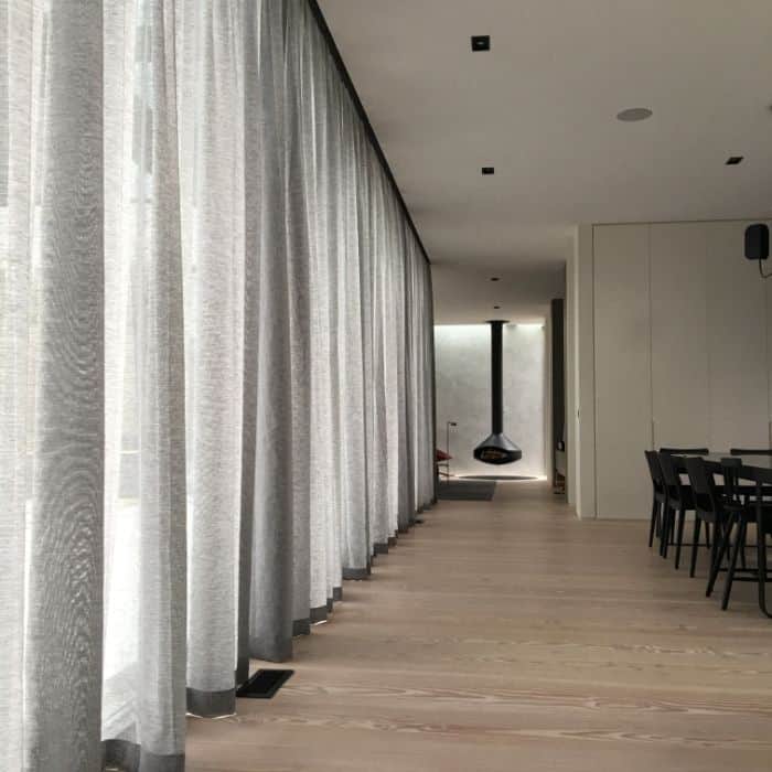 Roman Blinds & Curtains Melbourne - a room with wooden floors, light grey curtains, a fireplace and chairs
