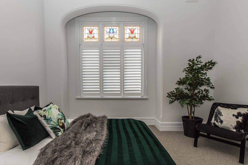 Plantation Shutters In Timber Or Aluminium - a bedroom with arch and windows with stained glass pains and shutters