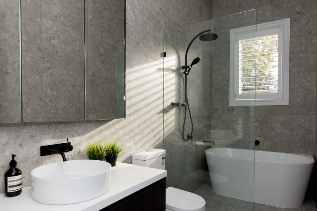 Plantation Shutters In Timber Or Aluminium - a bathroom with a shuttered window above the bath next to the shower head
