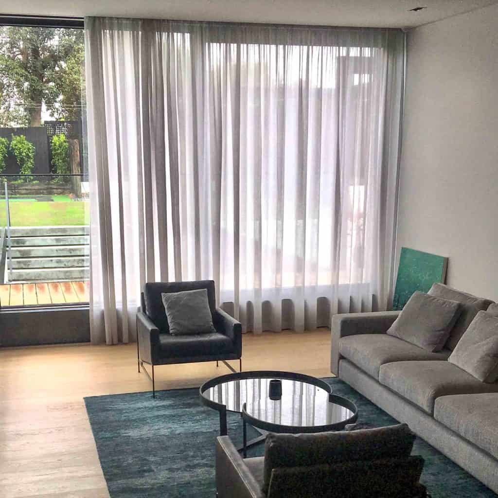 Roman Blinds & Curtains Melbourne - a room with couches and chairs, large windows are covered with long grey curtains