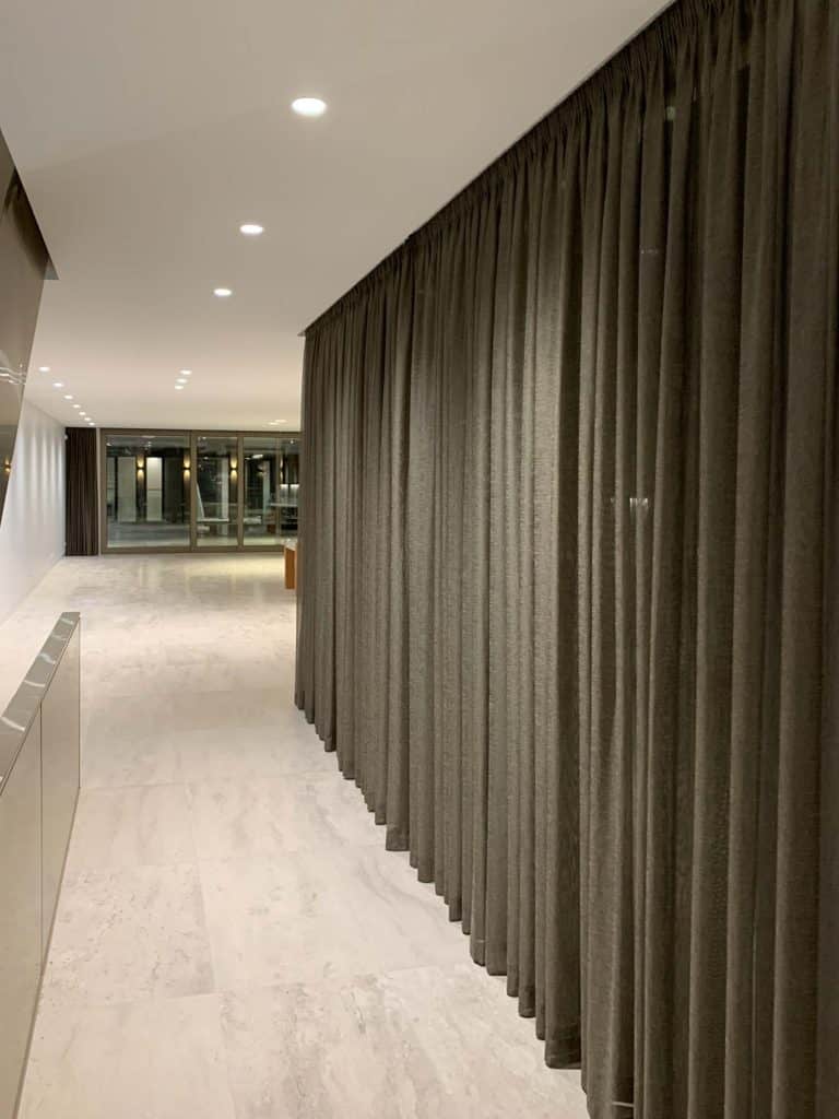 Roman Blinds & Curtains Melbourne - a long passageway with dark grey curtains and light marble floors