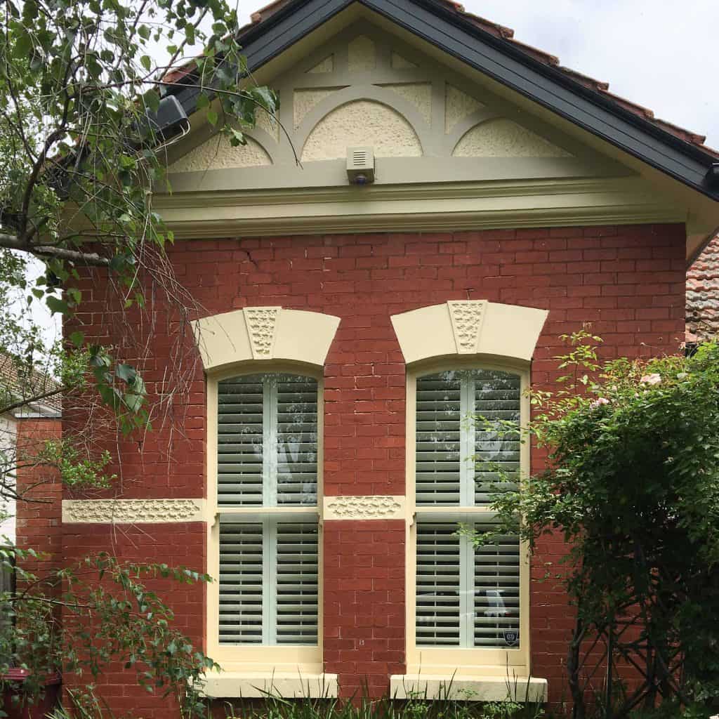 Plantation Shutters In Timber Or Aluminium - a red brick wall with two large windows that include inside shutters