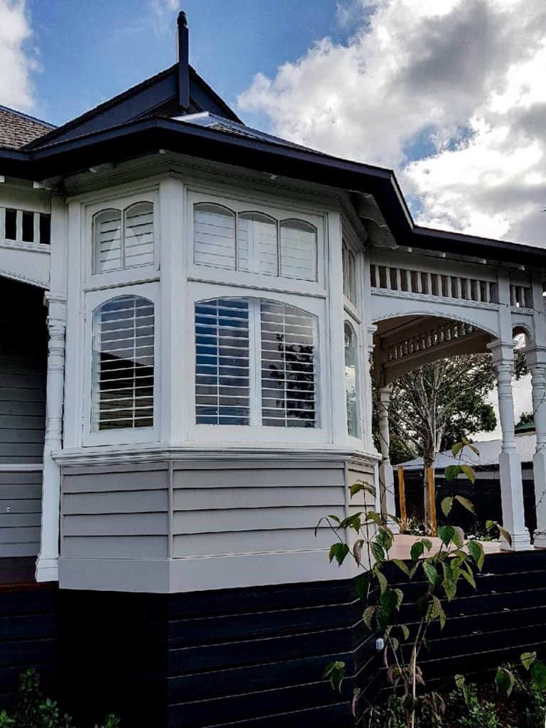 Plantation Shutters In Timber Or Aluminium - the outside view of a house with windows and a porch. Shutters are visible inside the windows