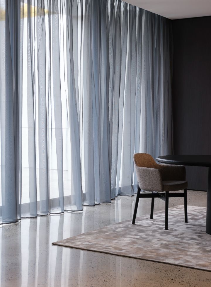 Roman Blinds & Curtains Melbourne - a dining room table with blue curtains and a carpet on the concrete floor