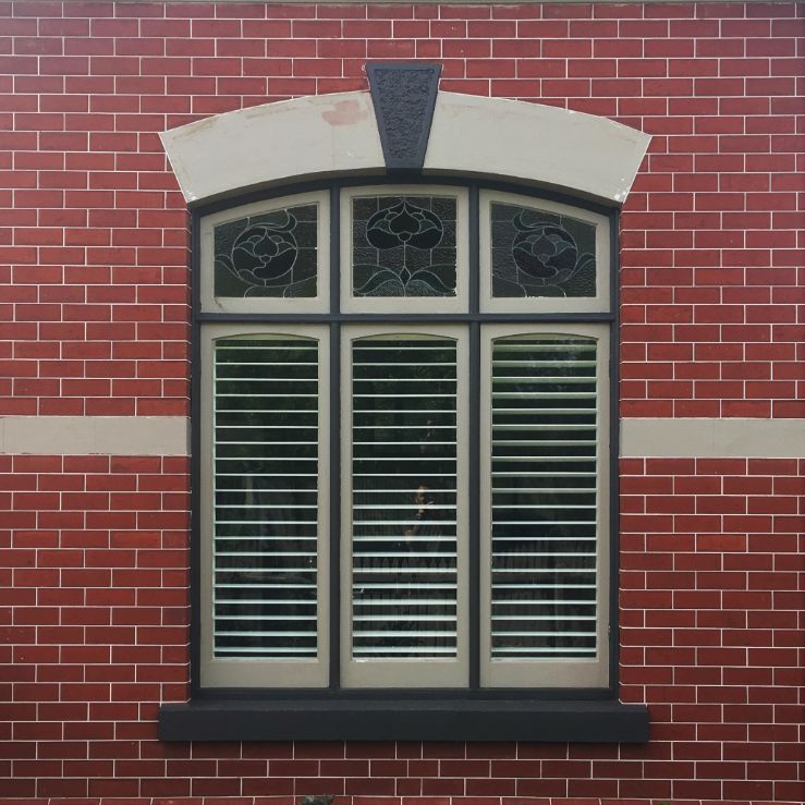 Plantation Shutters - beautiful plantation shutters in aluminium in a red-brick home with glass panes at the top of the window