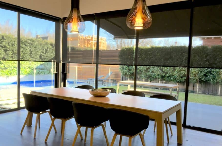 Motorised Blinds & Roller Blinds Melbourne - a large wooden dining table with big windows and dark blinds