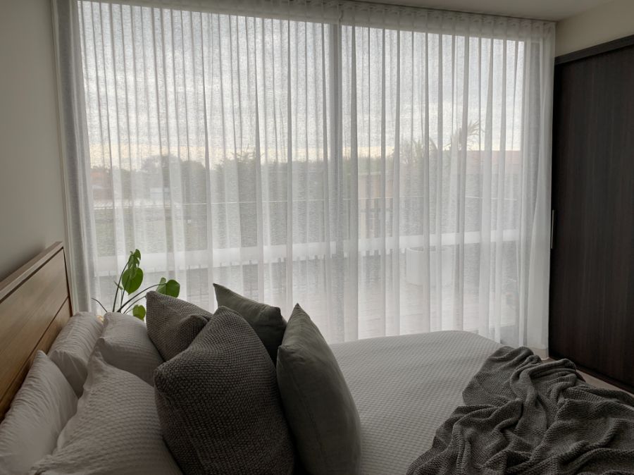 Motorised Blinds & Roller Blinds Melbourne - a bedroom with a double bed and large sliding rooms covered by a light curtain
