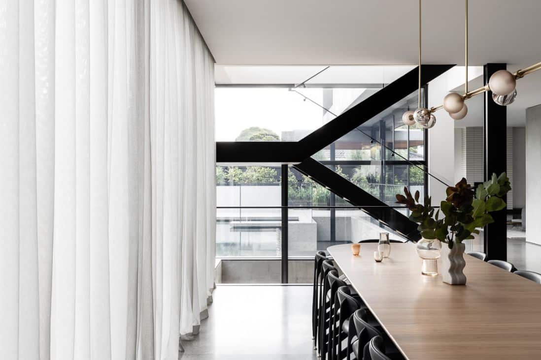 Roman Blinds & Curtains Melbourne - A lovely dining room with a see-through staircase in the background, protected by curtains