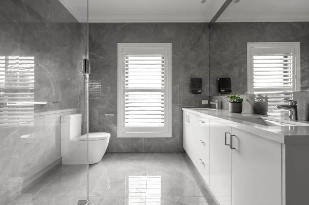 Plantation Shutters In Timber Or Aluminium - a bathroom with grey marble tiles on the floor and walls and a white framed window