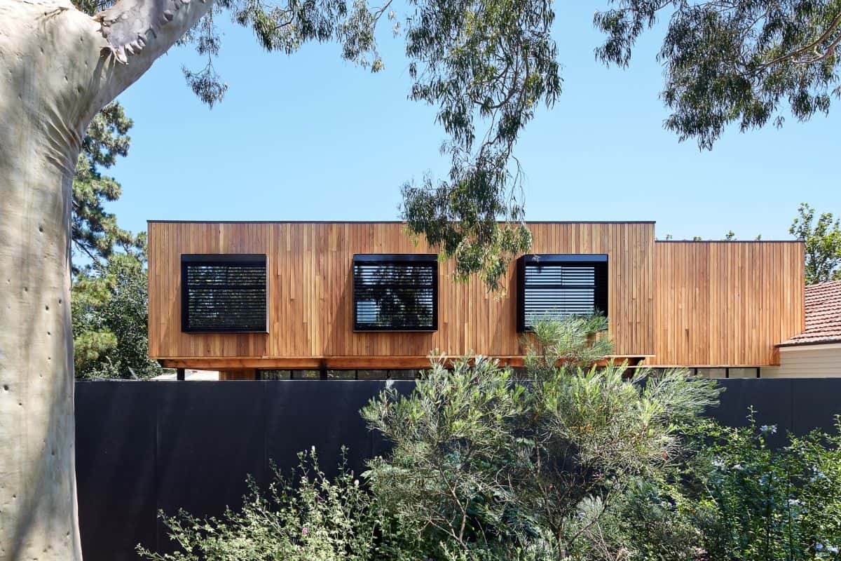 A wooden exterior home with dark roller blinds on the second floor of the building