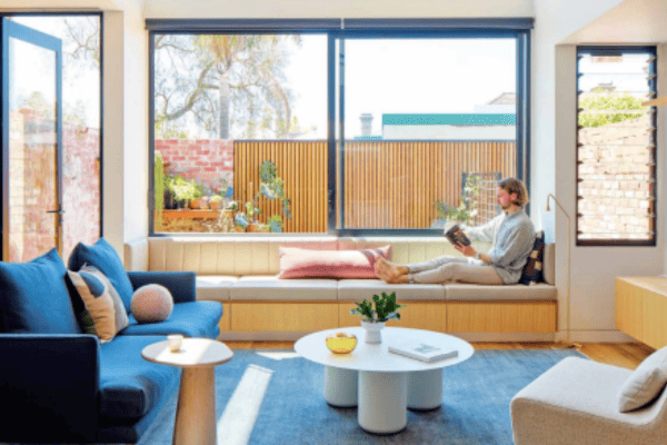 A man sitting on the couch with protection from the external sun due to roller blinds.