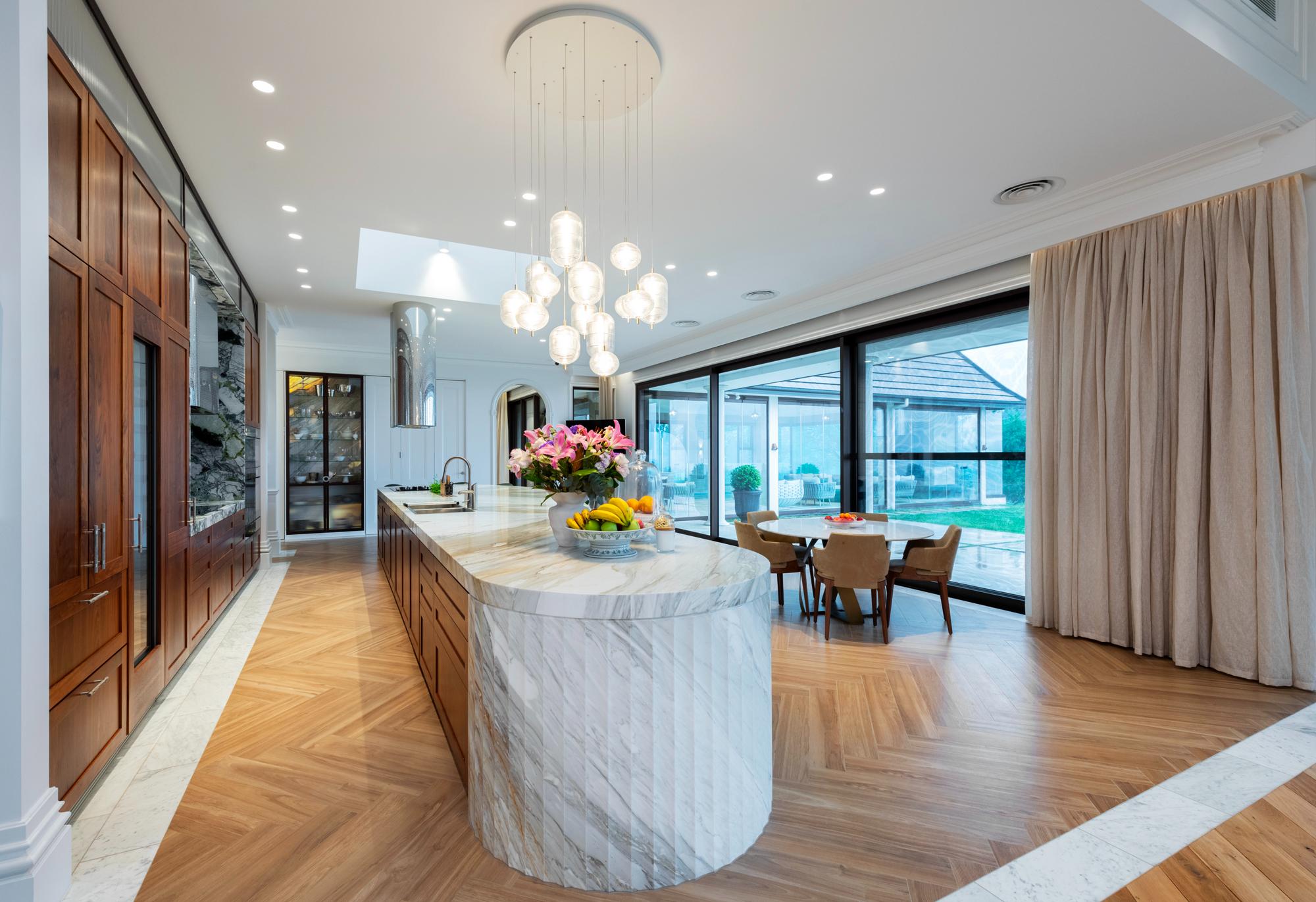 Large high end marble and timber kitchen with floor to ceiling curtains stacked to right along expansive window
