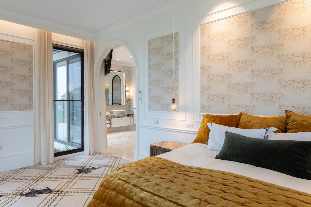 Bedroom featuring wainscoting and custom designed wallpaper and carpet featuring race horses with open sheer curtains