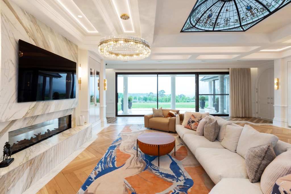 Elegant living space large picture windows looking into garden with floor to ceiling motorised curtains stacked to one side, large circular chandelier