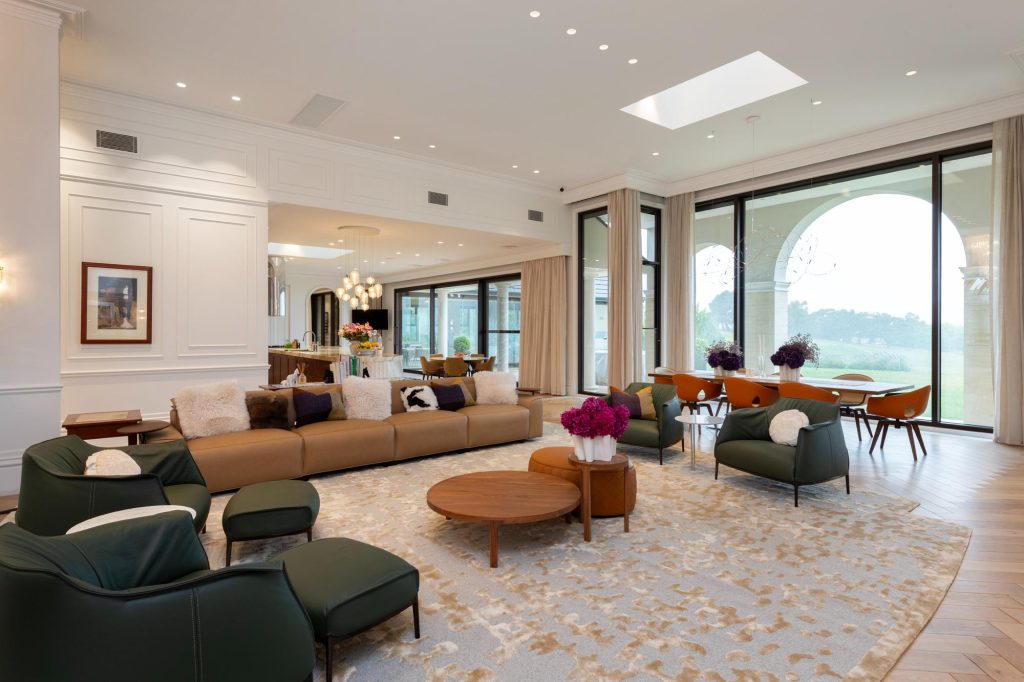 Living room and kitchen beyond with modern furniture and floor to ceiling sheer curtains on large windows with rural view