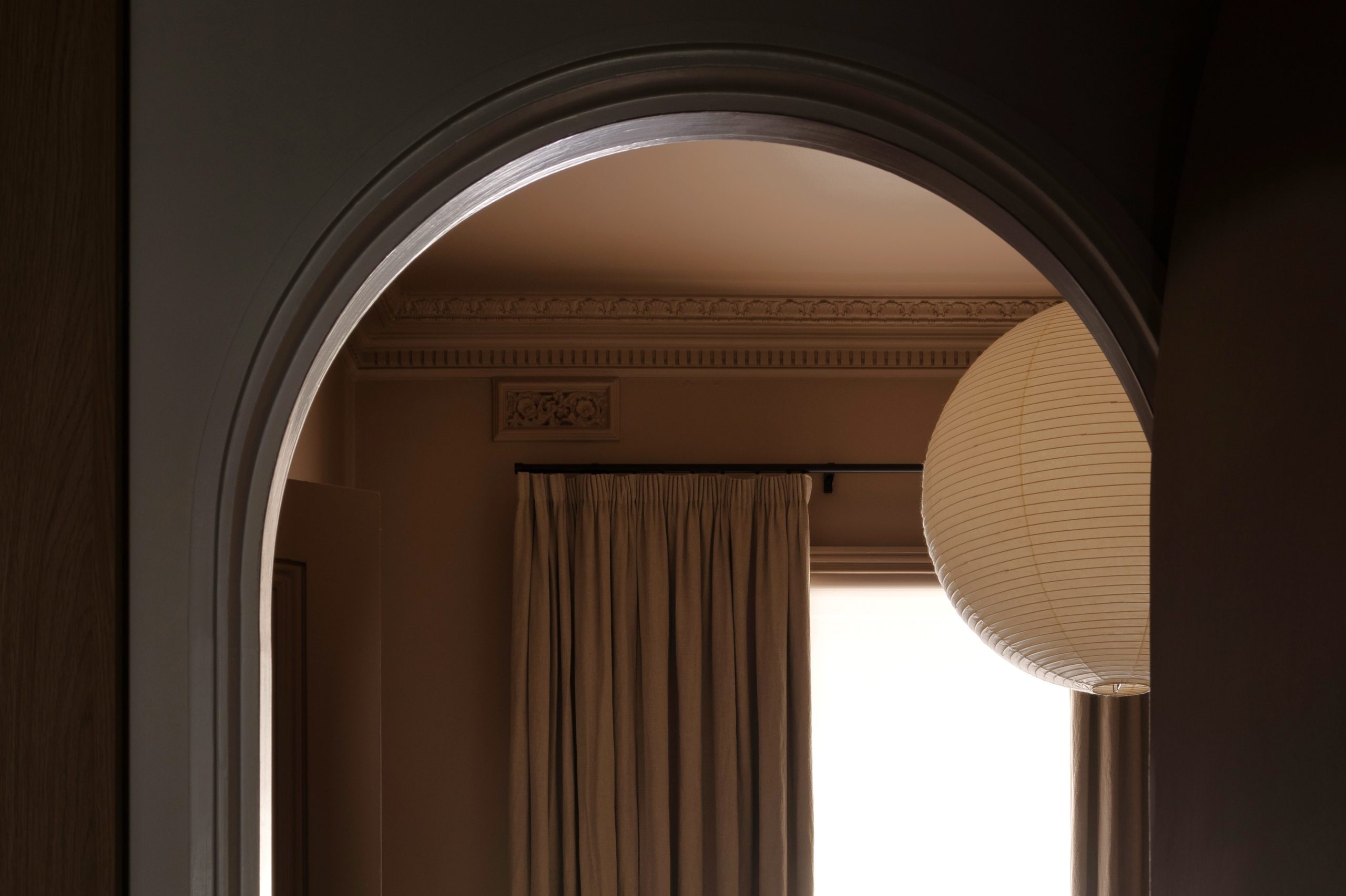 Looking through arched doorway into bedroom with custome window furnishings - pencil pleat banded curtains on black decorative rod in period home with ornate cornice