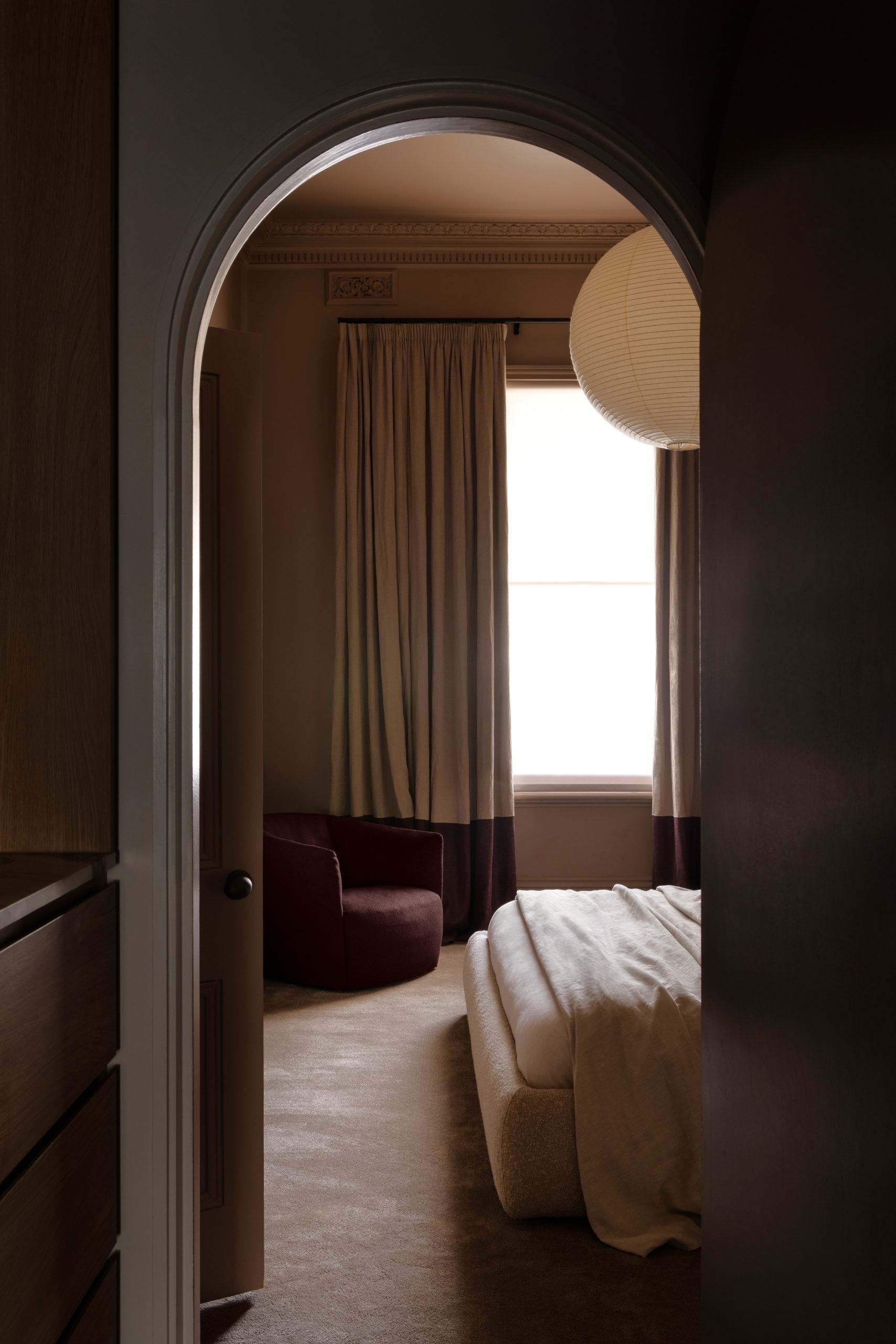 View through arched doorway into master bedroom of WD Residence Toorak showing custom window furnishings - pencil pleat banded curtains